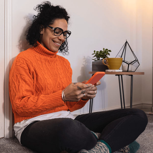Femme assise au sol et lisant son smartphone tout sourire